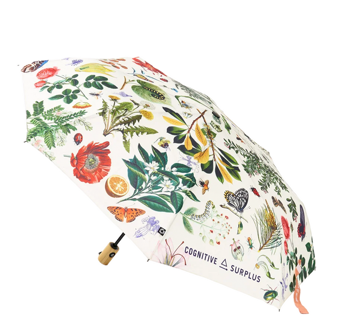 An open compact umbrella with a white background covered in colorful botanical illustrations, including flowers, leaves, butterflies, and birds. The handle is light wood with a black grip, and the brand name 'COGNITIVE SURPLUS' is printed near the lower right edge.