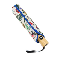 A closed folding umbrella with a cream-colored fabric cover decorated with a colorful botanical and bird pattern, featuring a bright blue trim and a light bamboo handle.