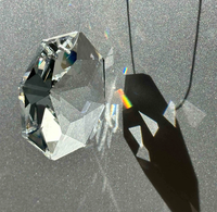 A clear faceted crystal prism casting sharp shadows and a rainbow spectrum on a textured gray surface.