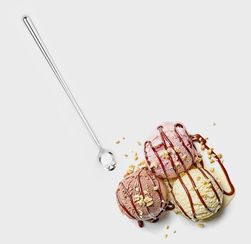 Three scoops of ice cream on a light gray background, topped with chocolate drizzle and crushed nuts, alongside a long metal spoon.