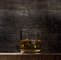 A small glass tank with yellow fish and a striped round fish sits on a dark wooden shelf against a shadowy wall, creating a quiet, moody scene.