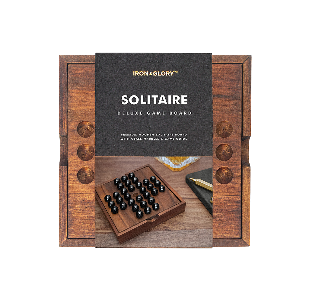 A boxed Iron & Glory wooden Solitaire deluxe game board, shown with a walnut-colored peg board and black glass marbles; refined, premium presentation.