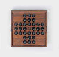 A wooden tabletop peg solitaire board with black marbles in a cross-shaped pattern and one empty center hole, photographed against white; calm, handcrafted feel.