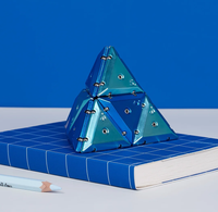 Geode chrome magnetic triangular pieces assembled into a pyramid, sitting on top of a book and next to a pencil. 