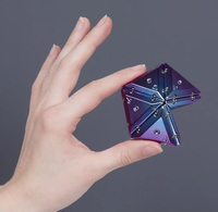 A hand holding a small, star-shaped iridescent purple and blue object with metallic silver rivets against a solid dark gray background.