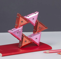 Pink and orange chrome triangular magnetic pieces assembled into a star shape standing on top of a notebook. 