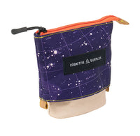 A small zippered pouch with a dark purple starry space print, an orange zipper, a black brand patch reading 'COGNITIVE SURPLUS', and a beige fabric flap at the bottom, shown on a white background.