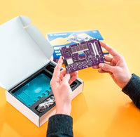 Person holding a purple circuit board over an open box on a yellow background