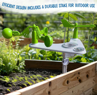 A green and white outdoor weather station with a wind vane, anemometer, and thermometer, shown planted in a wooden raised garden bed with a blurred garden background. Text at the top reads 'EFFICIENT DESIGN INCLUDES A DURABLE STAKE FOR OUTDOOR USE'.