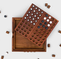 A wooden board is open and the lid is resting on top with white, black and patterned pegs on it. Wooden pegs are scattered around the board. 