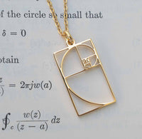 Gold necklace with a Fibonacci spiral pendant on a paper background.