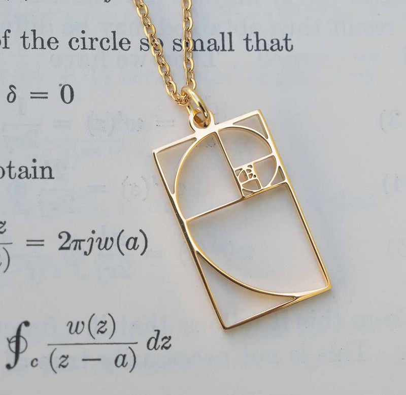 Gold necklace with a Fibonacci spiral pendant on a paper background.