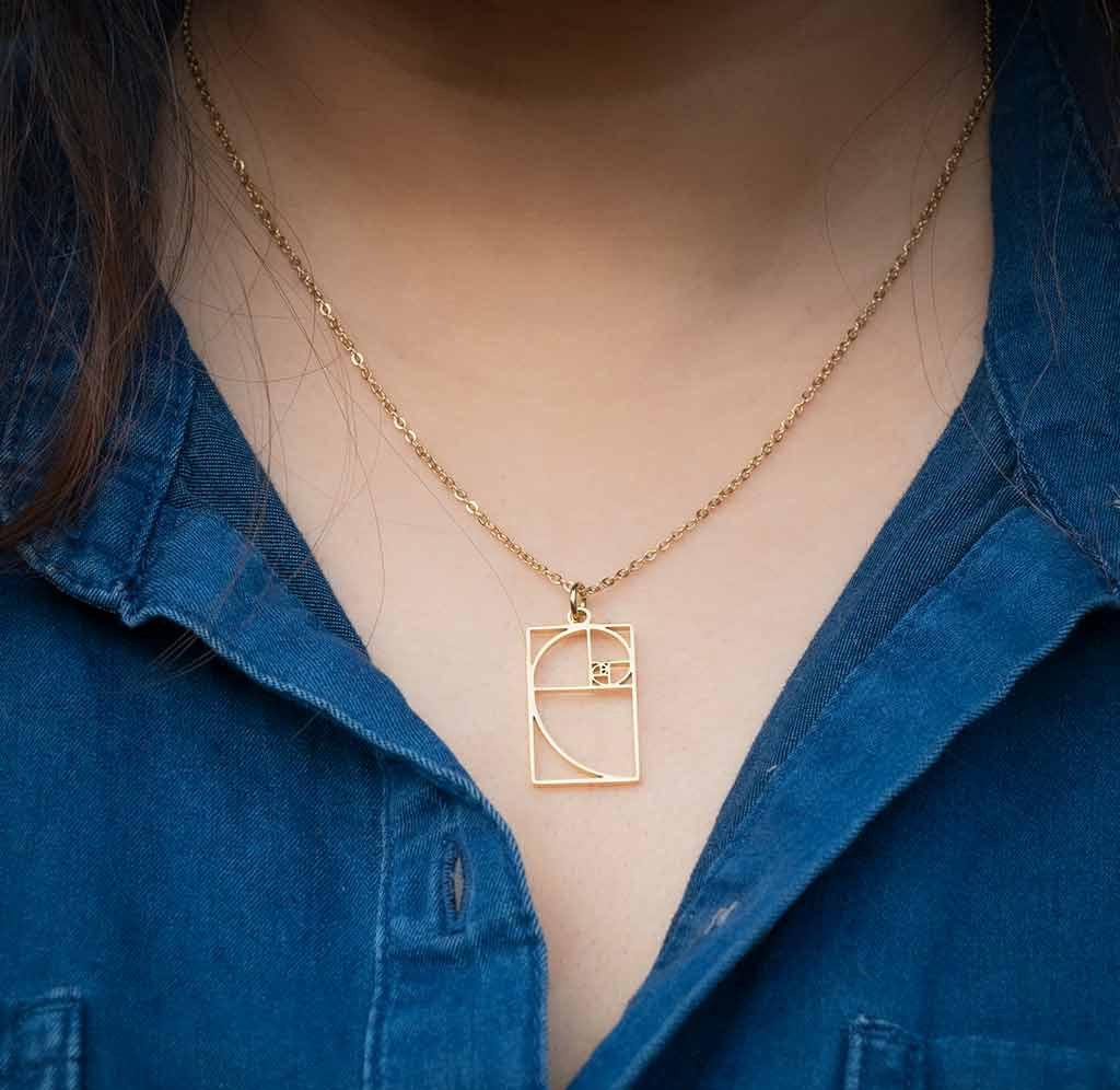 Gold necklace with a geometric pendant worn by a person in a blue shirt.