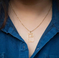 Gold necklace with a geometric pendant worn by a person in a blue shirt.