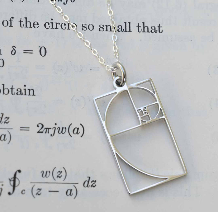 Silver necklace with a Fibonacci spiral pendant on a paper background.
