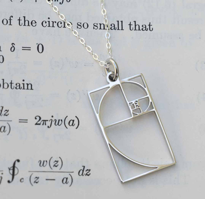 Silver necklace with a Fibonacci spiral pendant on a paper background.