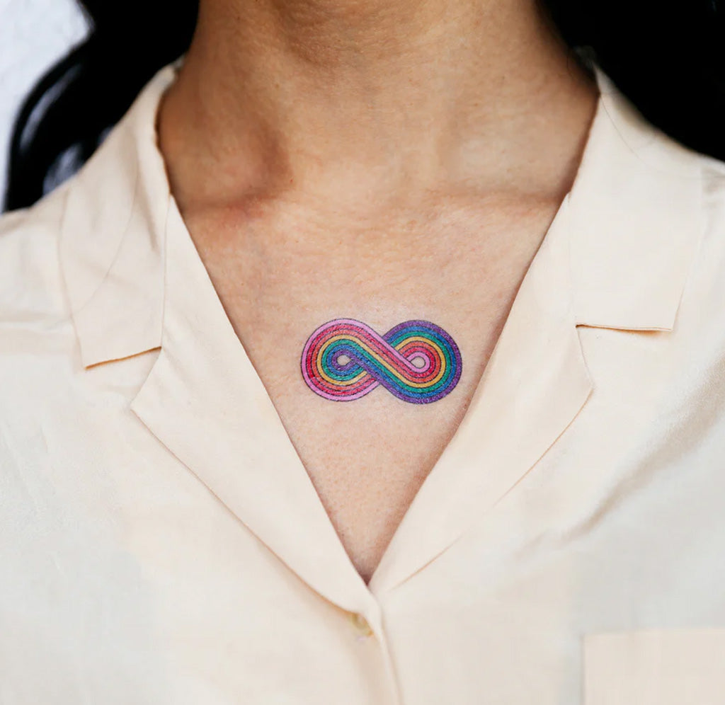 A close up of a person's upper chest with a rainbow infinity tattoo in the center. 