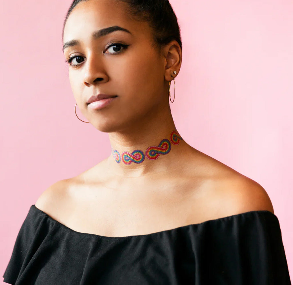 A person has multiple rainbow infinity tattoos placed around her neck. 