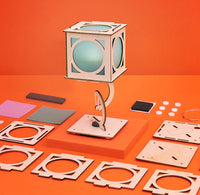 Wooden lantern on an orange background with pieces around it. 