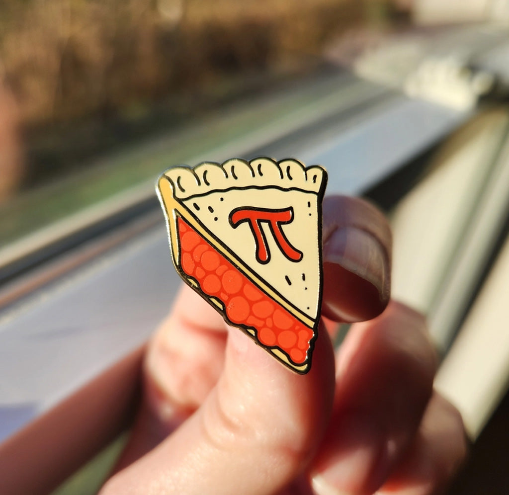 Someone holding the Pi Pie Slice pin in their hand in front of a window. 