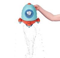 A hand holding a blue and red rocket shaped bath toy that is pouring water from the bottom. 