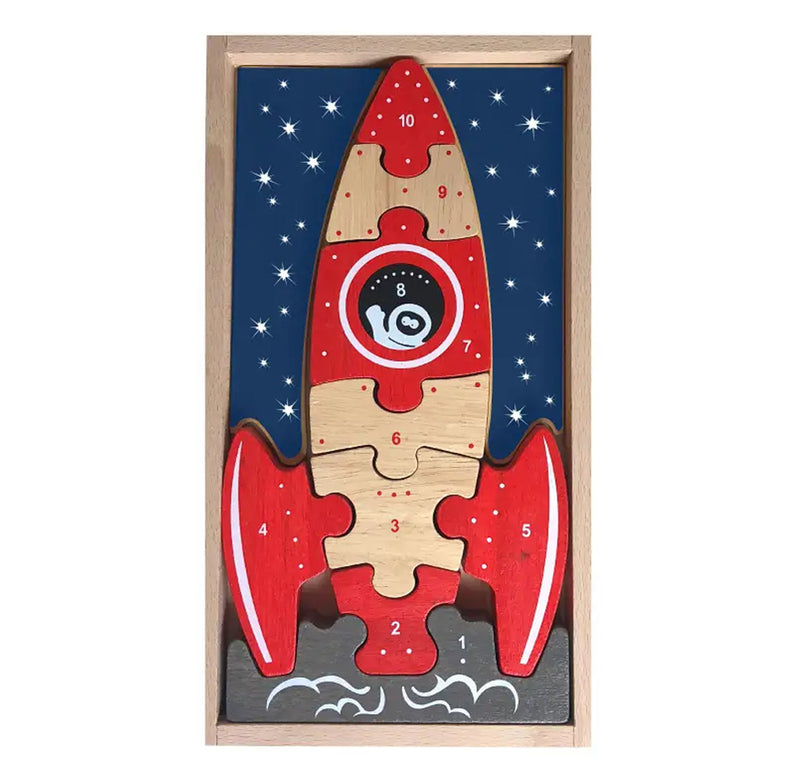 Red and natural-colored wooden rocket ship with a number count down on the pieces. An astronaut waves through the window as the rocket as white smoke bellows at the bottom. It sits in a wooden box surrounded by blue sky and stars.