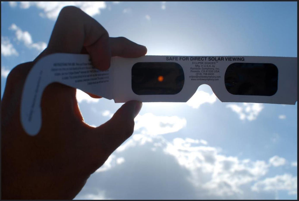 White paper eclipse glasses pointing toward the sun in the sky showing the eclipse through the lens.