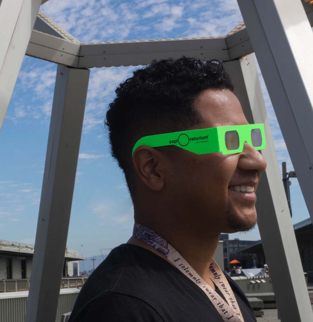 A man standing in profile underneath the Buckyball exhibit wearing lime green diffraction glasses.