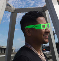 A man standing in profile underneath the Buckyball exhibit wearing lime green diffraction glasses.