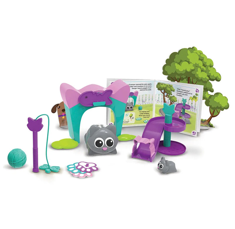 Two gray kittens sit in their purple, teal and pink playset area, complete with a slide, yarn, butterfly cat toy, cat house, and trees.