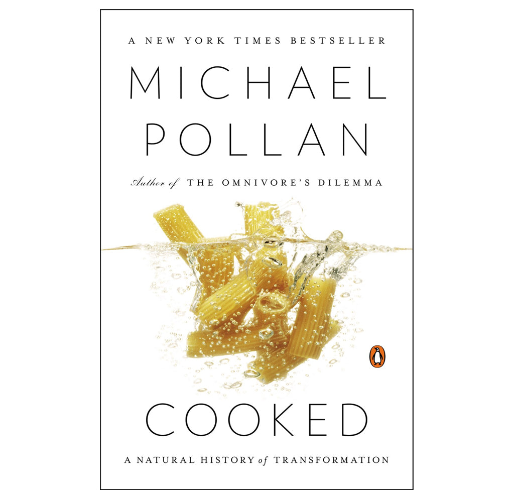  "Cooked" is a paperback book; several rigatoni pieces are slowly boiling in the water with air bubbles and splashes against a white background.  