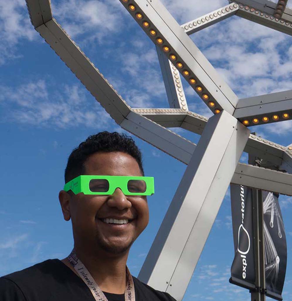 A man stands underneath the Buckyball exhibit wearing lime green diffraction glasses.