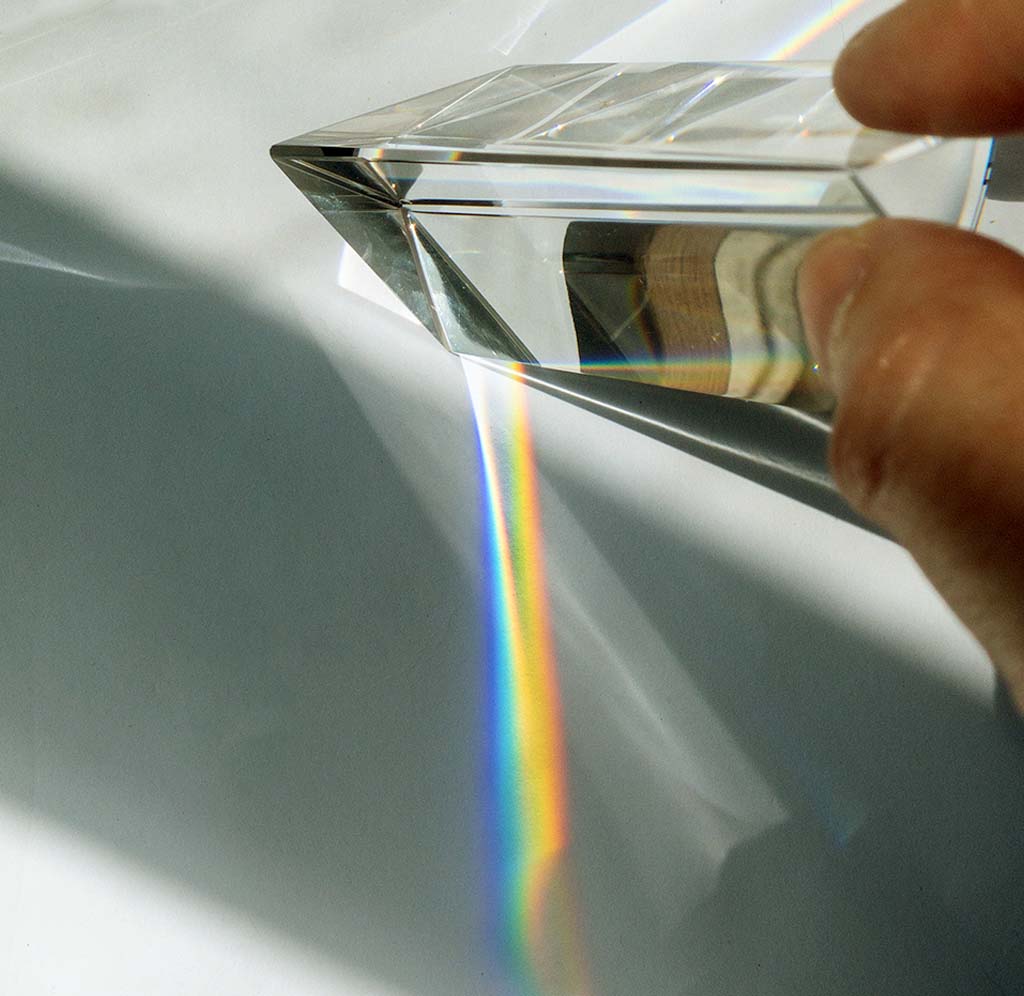 A triangular glass prism is refracting light waves to make a rainbow.