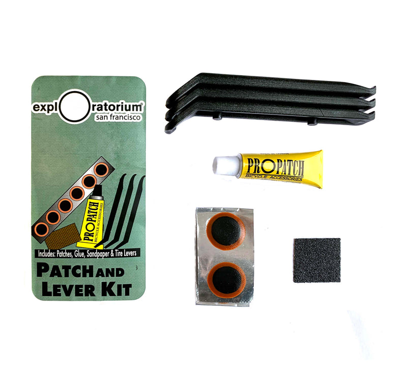 There is a rectangular-shaped plastic box with an image in green, yellow, silver, and white with the kits items on it. There are three black tire levers, a roll of patches, sandpaper, and ProPatch glue sitting next to it.