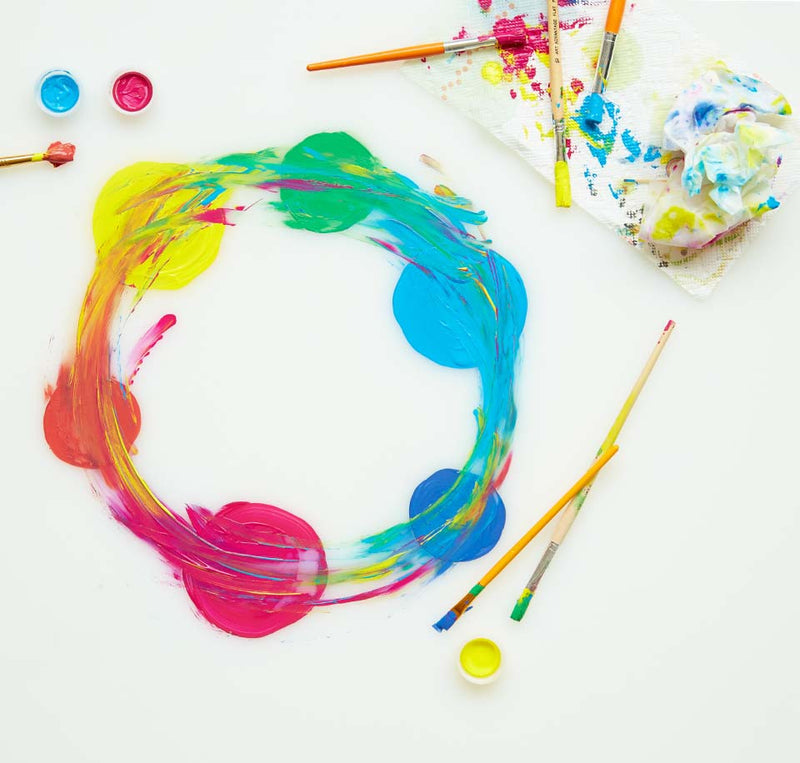 Small circles of different colored paints blended into each other to create a new ring; brushes and paint paraphernalia dotted about the ring.