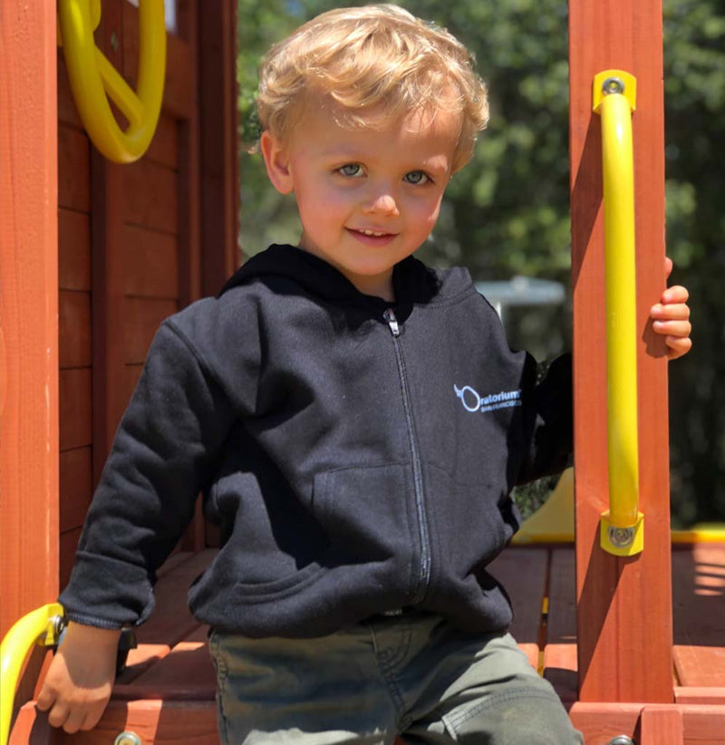 Toddler on playset wearing a black hoodie with Exploratorium on the front in white.