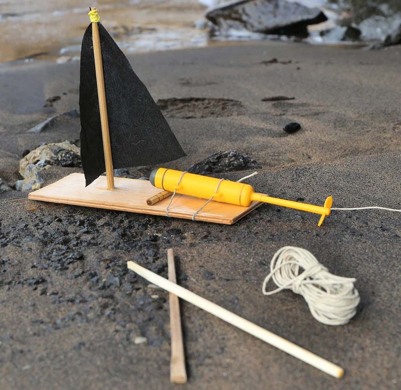 A motorboat made with wood with a black sail and the yellow motor kit sits on a beach.