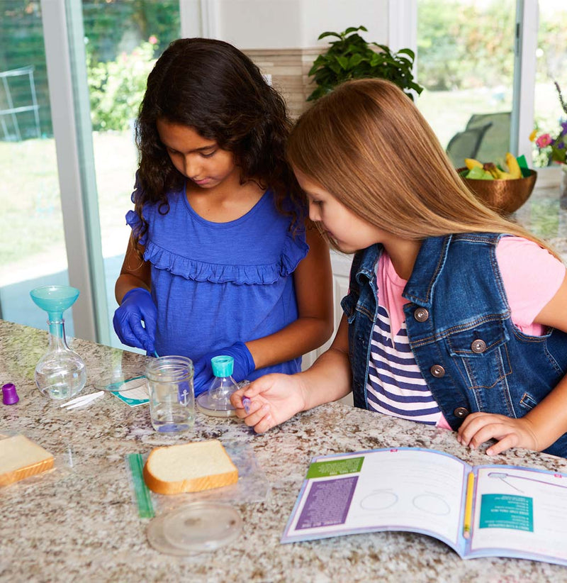 Two young girls are standing at a counter experimenting with bread.