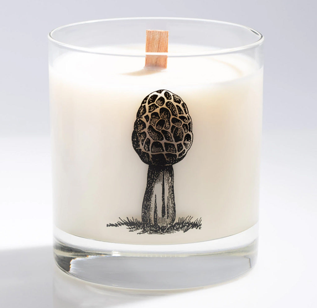 A morel mushroom in black is featured on this Whisky glass candle holder. A white candle with a wooden wick sits inside.
