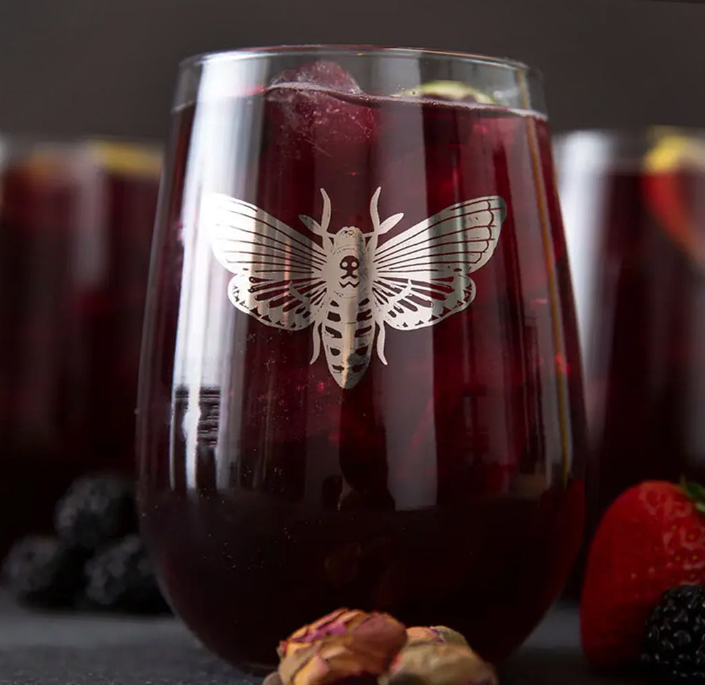 A stemless wine glass filled with red sangria; a silver moth in metallic platinum ink on the front.