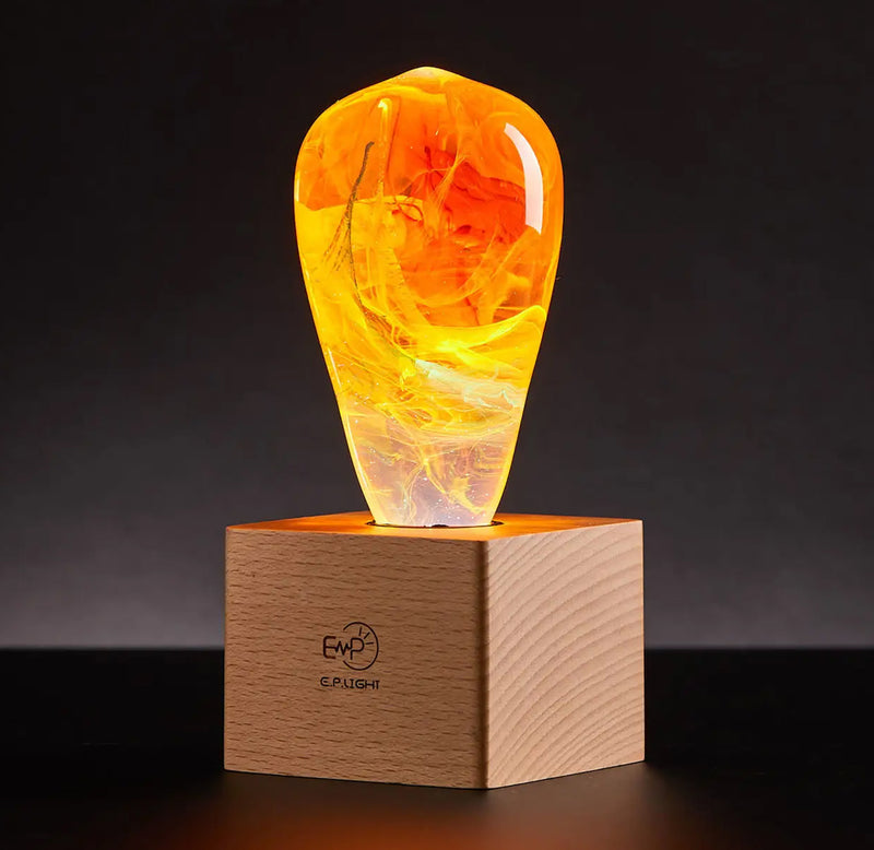A handmade glass bulb with orange, red, and swirling yellow colors sits atop a square wood lamp base.