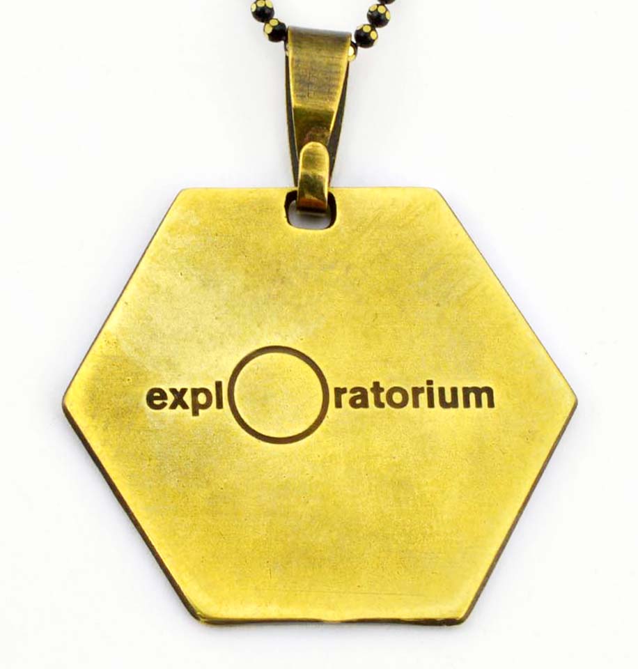    Golden Hexagon pendant from the back with the Exploratorium logo engraved.