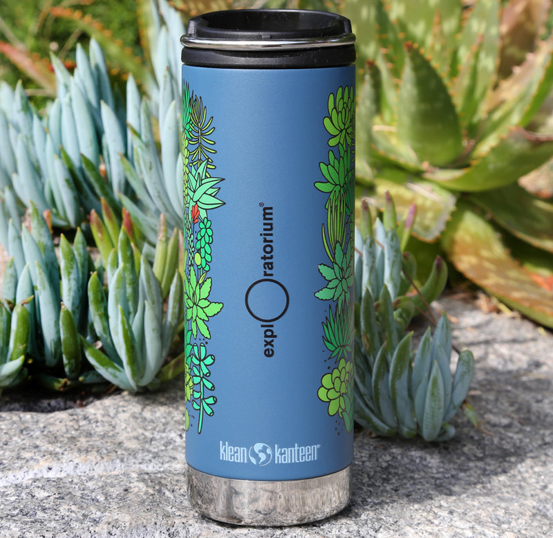 A tall, slender blue water bottle with a black lid, plants of many shades of green wrapped around the outside, and the Exploratorium logo in black down the middle.