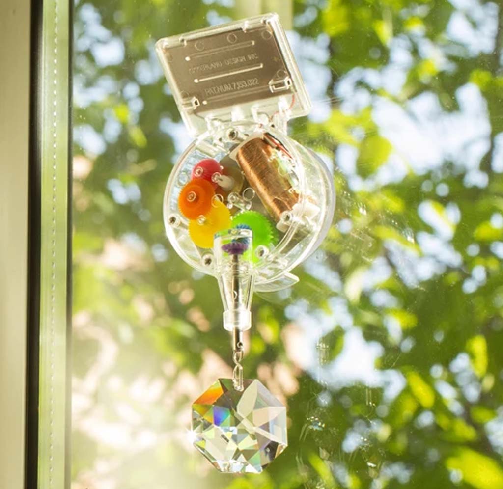 The sunlight is shining, a solar-powered Swarovski crystal spinning at the bottom of a see-through colorful gear motor attached to a window.
