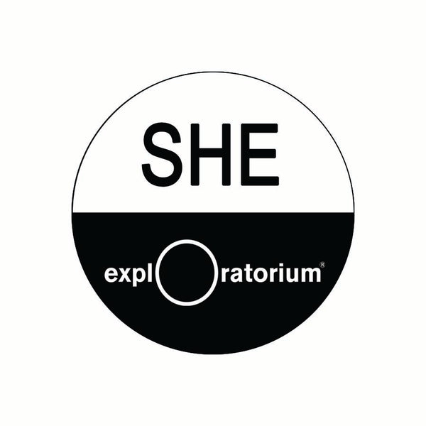 She pronoun pin in all caps in black text against a white background on the top half of the pin. Exploratorium in white text against a black background.