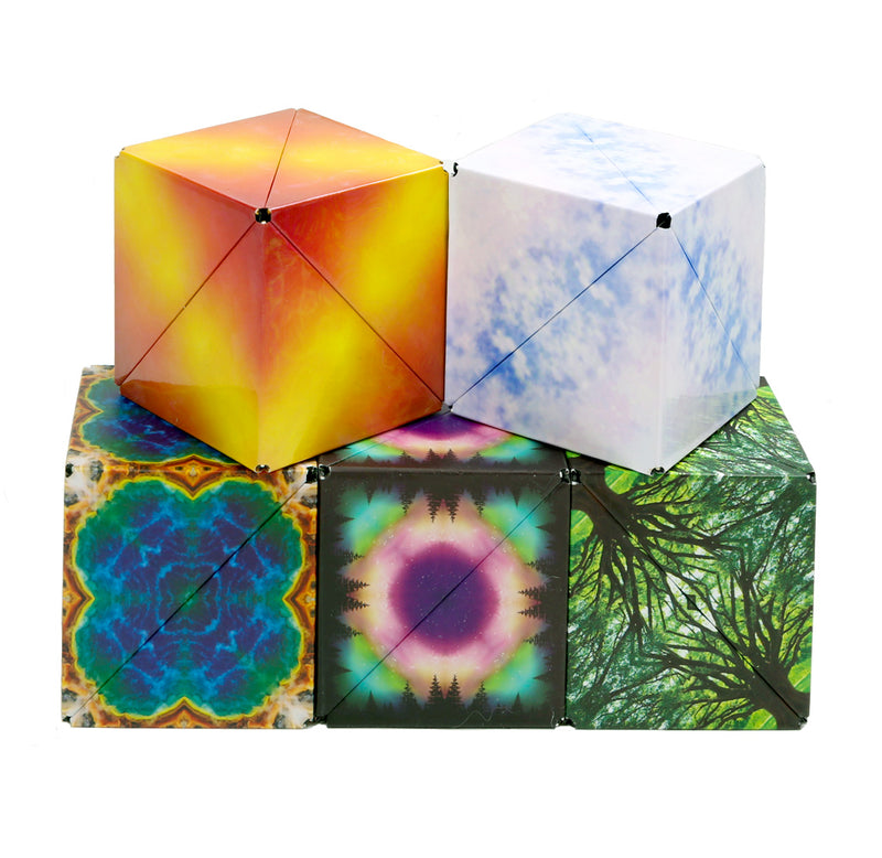 Five Shashibo cubes sit in a pyramid shape, with three on the bottom and two on the top. The top two cubes are yellow & red and blue & white. The three on the bottom are earth elements, aurora borealis, and green trees.