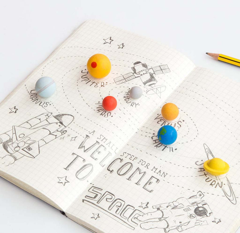 A notebook is opened up with a drawing in pencil of the night sky; each planet eraser has its own spot in colorful, yellows, reds, blues, and white.