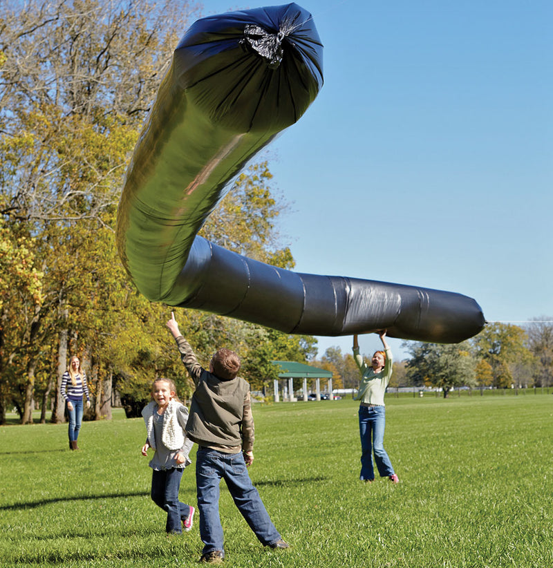 A giant black snake-shaped balloon is floating above three children in a park setting.