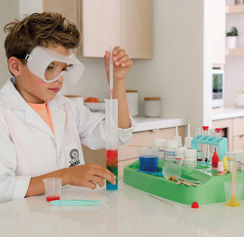 A child is experimenting with a large test tube with different colored liquids stacked on top of each other. Science-related tools are next to them on the table.