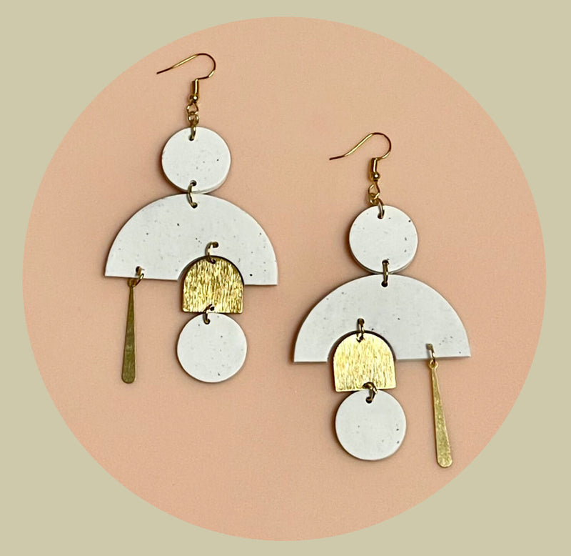  The earrings are white and gold with little black dots like vanilla bean seeds of circles, semi-circles, half ellipses, and dangling linear shapes.